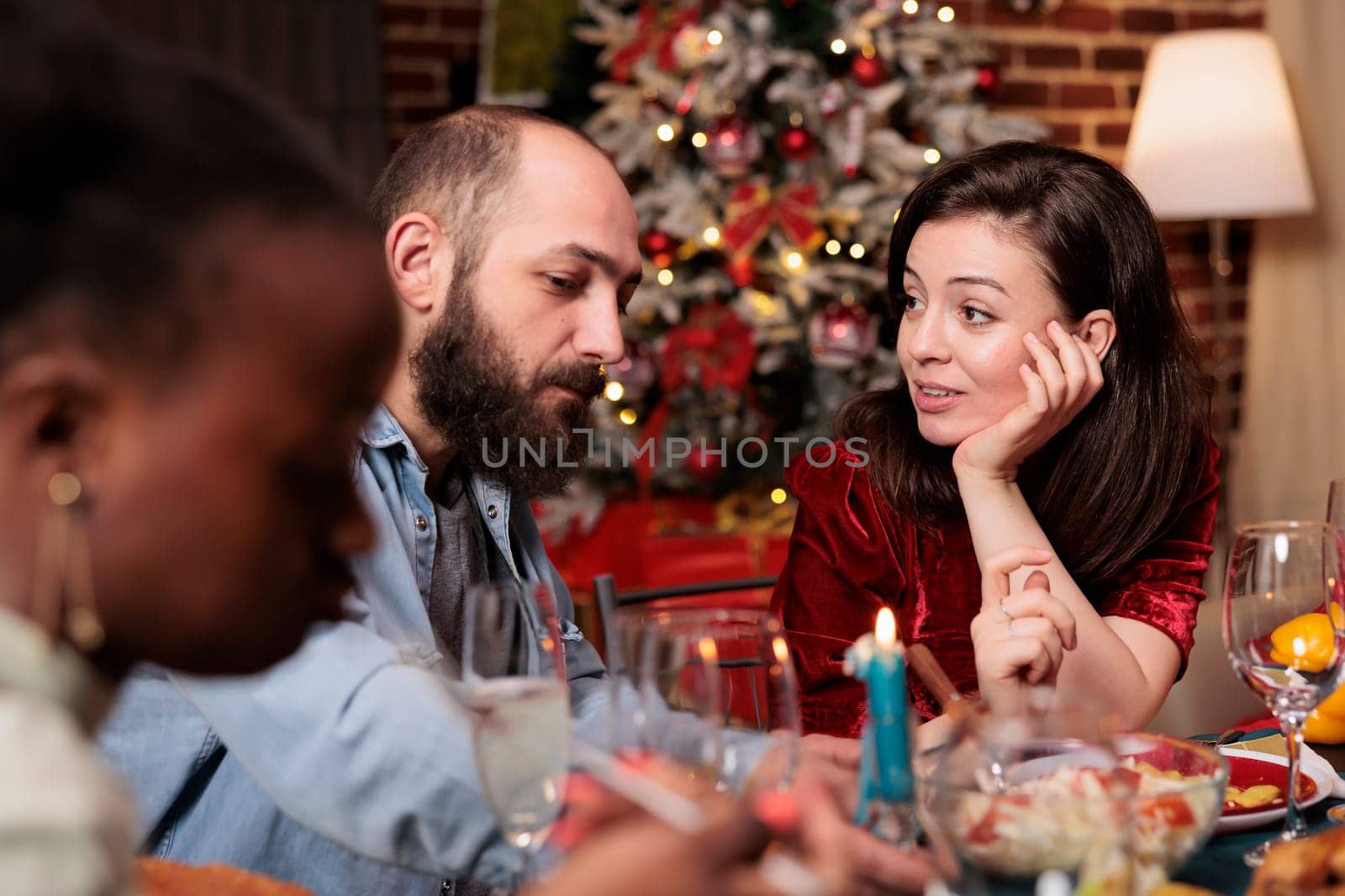 People enjoying christmas eve holiday with family, gathering at dinner table with friends. Diverse persons enjoying winter celebration in december with homemade meal and alcohol for xmas.