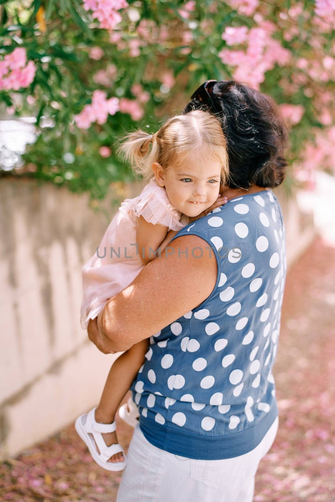 Granny with a little girl in her arms stands near a blooming oleander. Side view. High quality photo