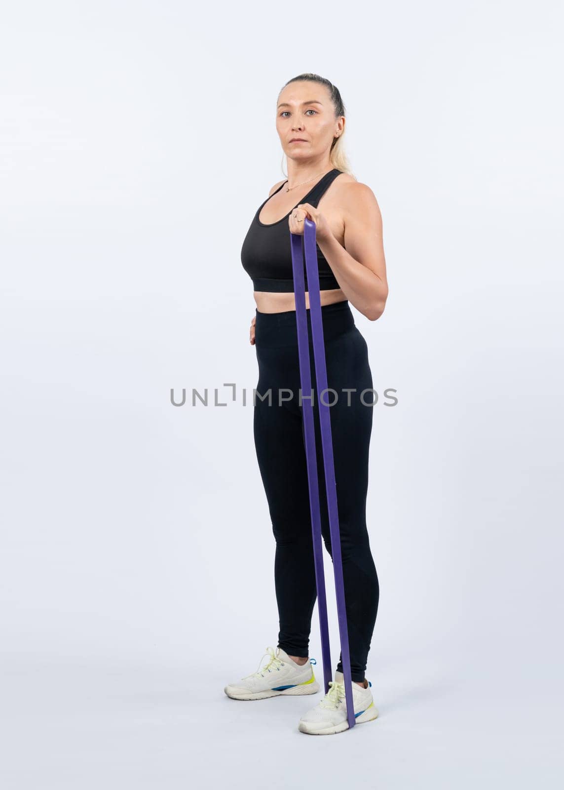 Full body length shot athletic and sporty senior woman with fitness resistance band on isolated background. Healthy active physique and body care lifestyle after retirement. Clout