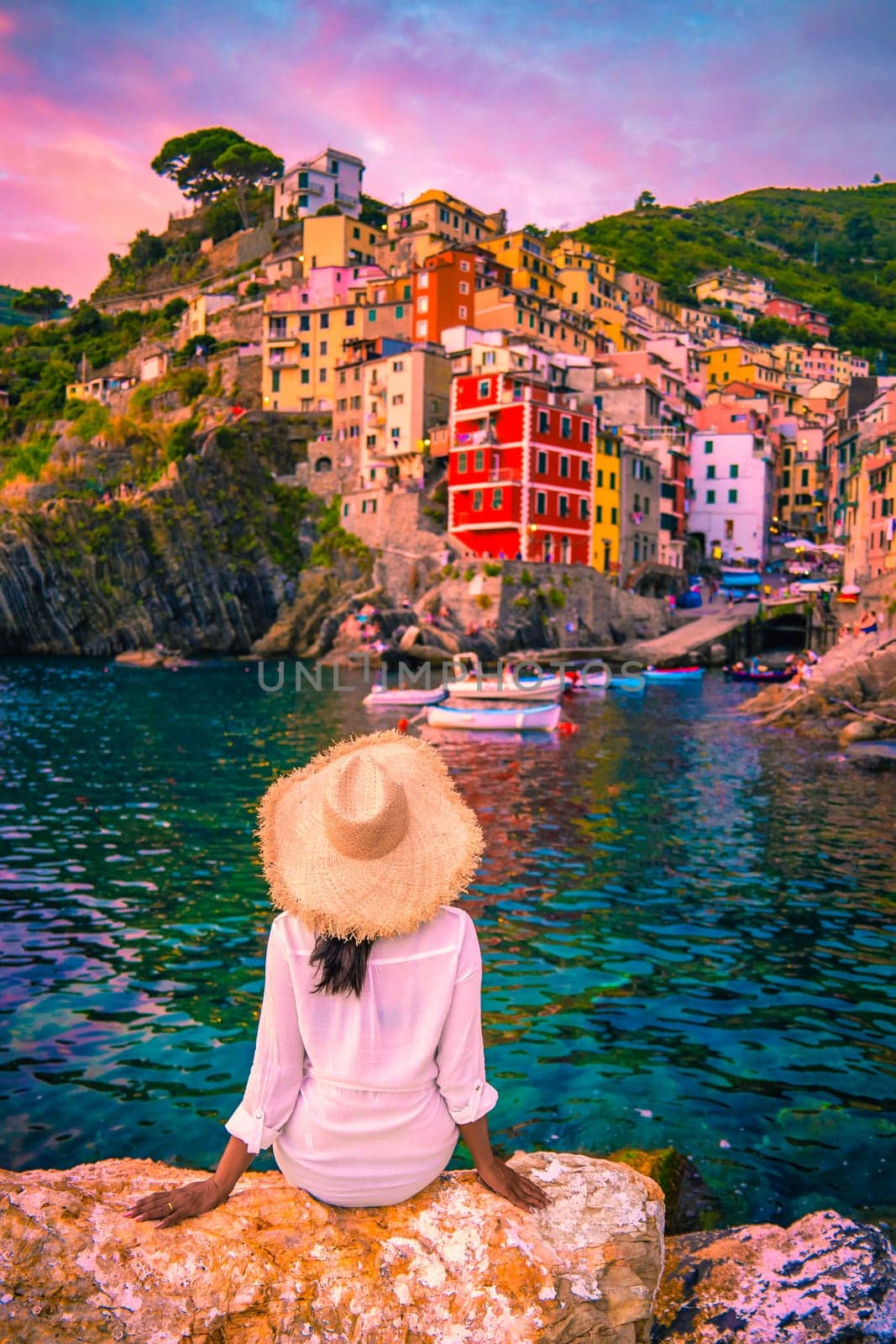 Riomaggiore Cinque Terre Italy, colorful village harbor front by the ocean, young Asian woman watching the sunset at waterfront looking out over Riomaggiore village Cinque Terre Italy