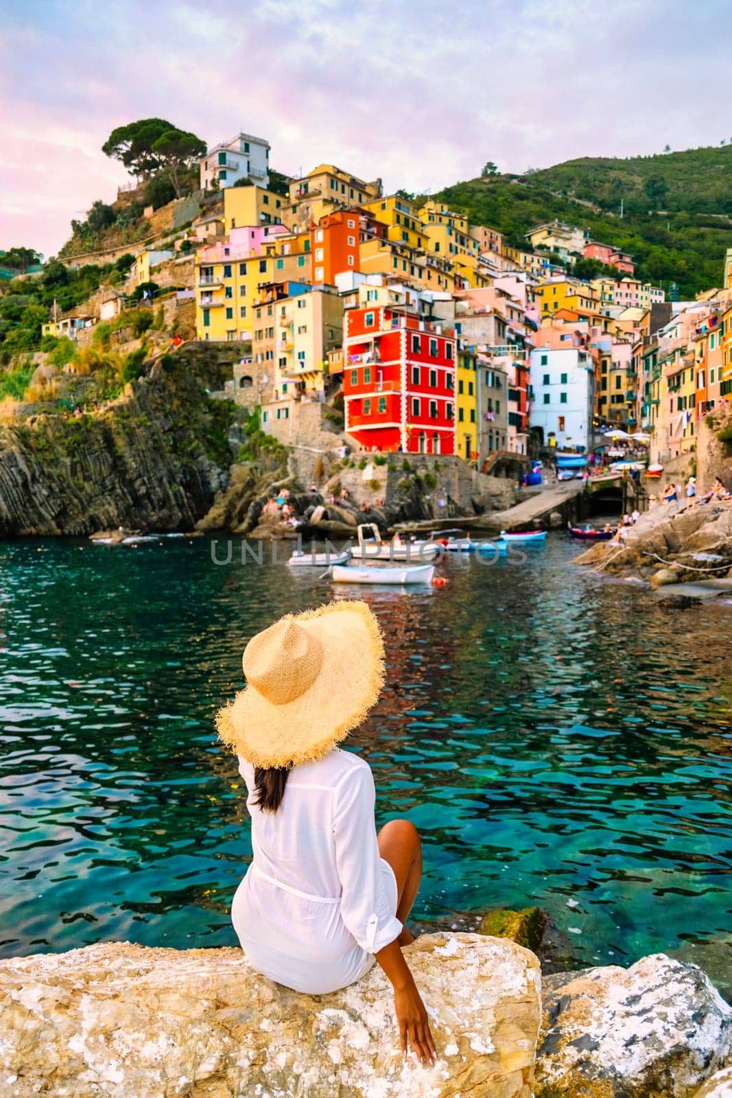 Riomaggiore Cinque Terre Italy , colorful village harbor front by the ocean, young woman watching sunset by fokkebok