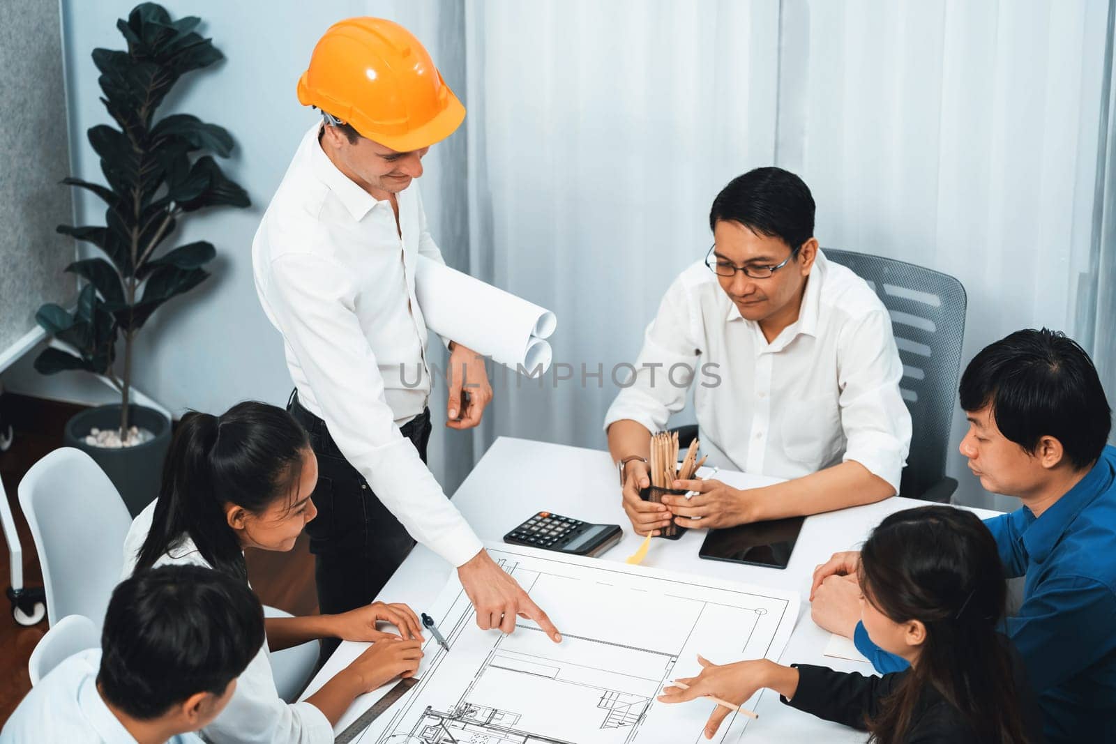 Diverse group of civil engineer and client working together on architectural project, reviewing construction plan and building blueprint at meeting table. Prudent