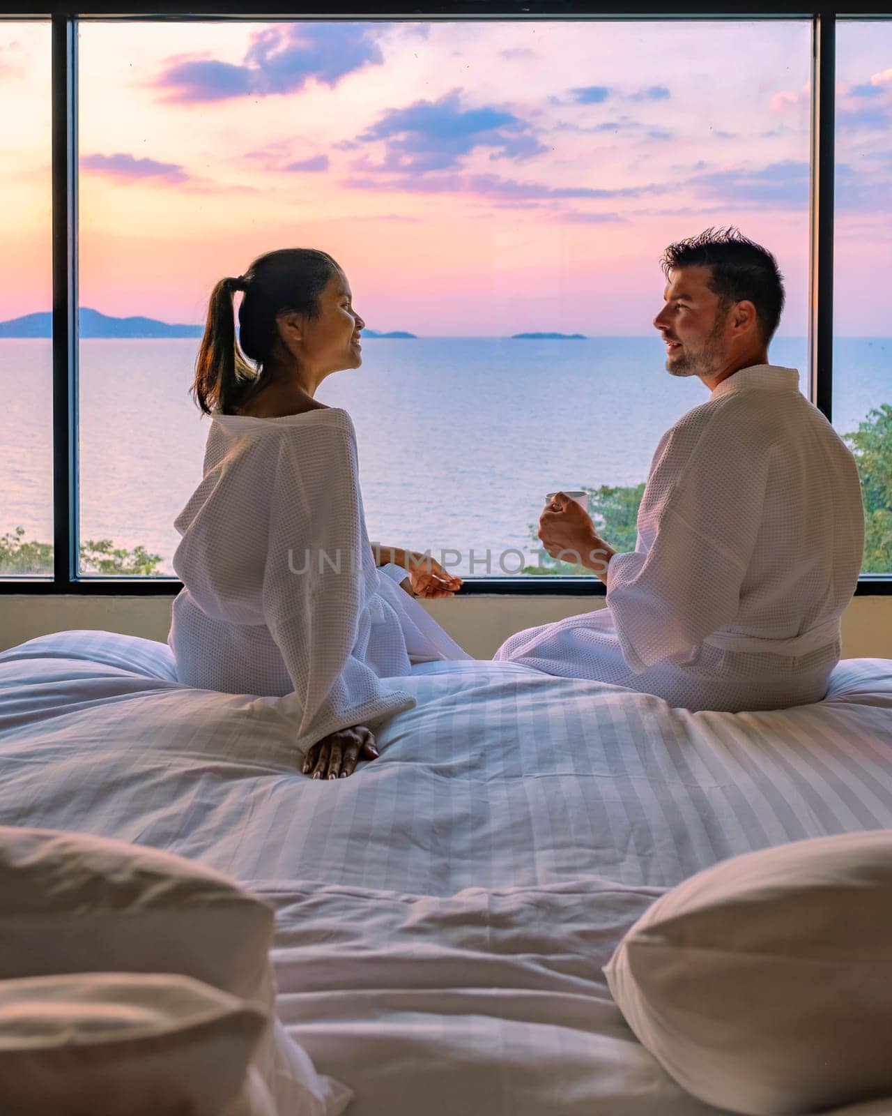 couple man and woman in front of bed in the bedroom during sunrise drinking a cup of coffee by fokkebok