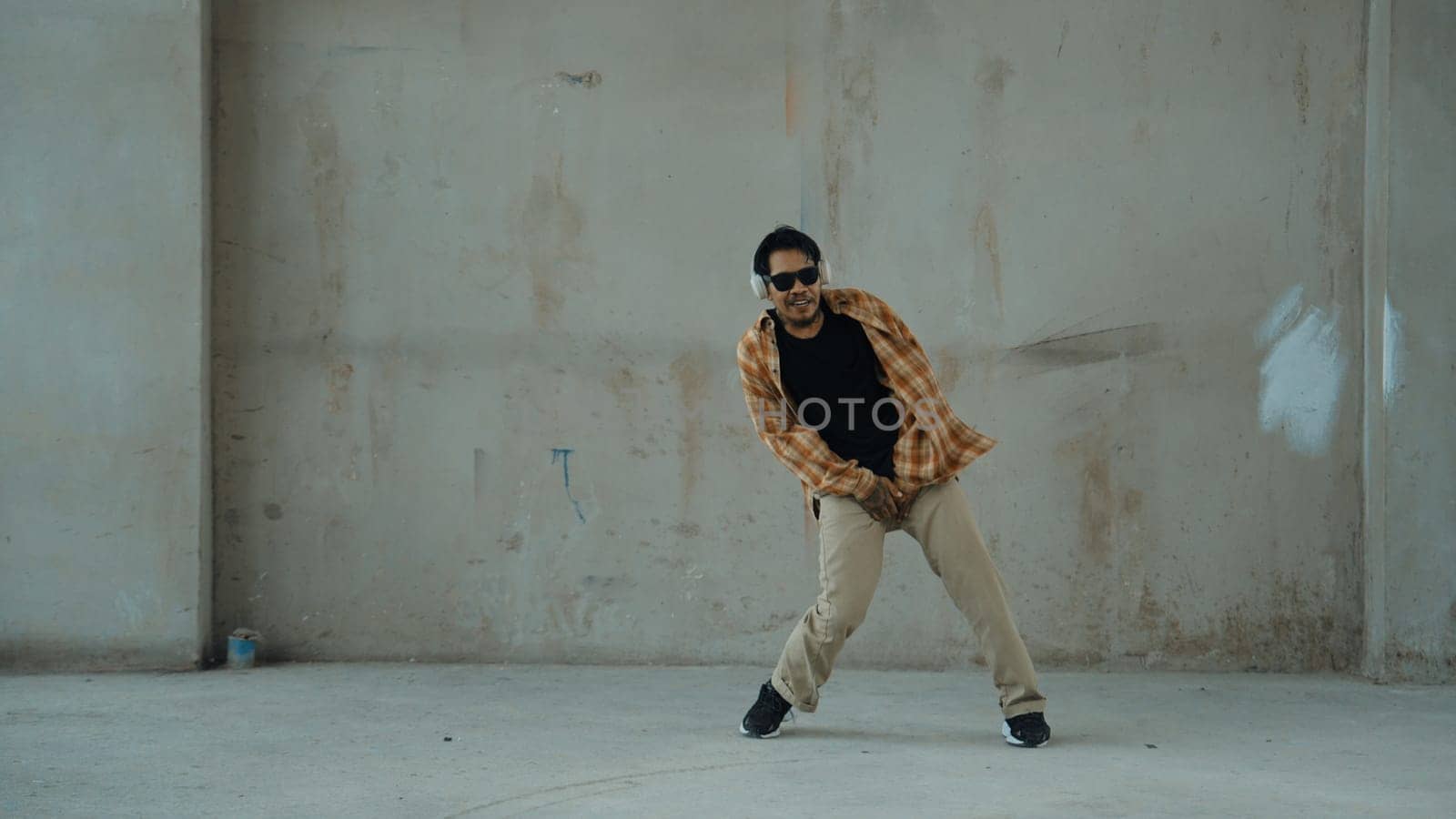 Attractive hispanic dancer in casual look practice street dance while listen music from headphone at cement background. Motion shot of break dancing performance. Outdoor sport 2024. Endeavor.