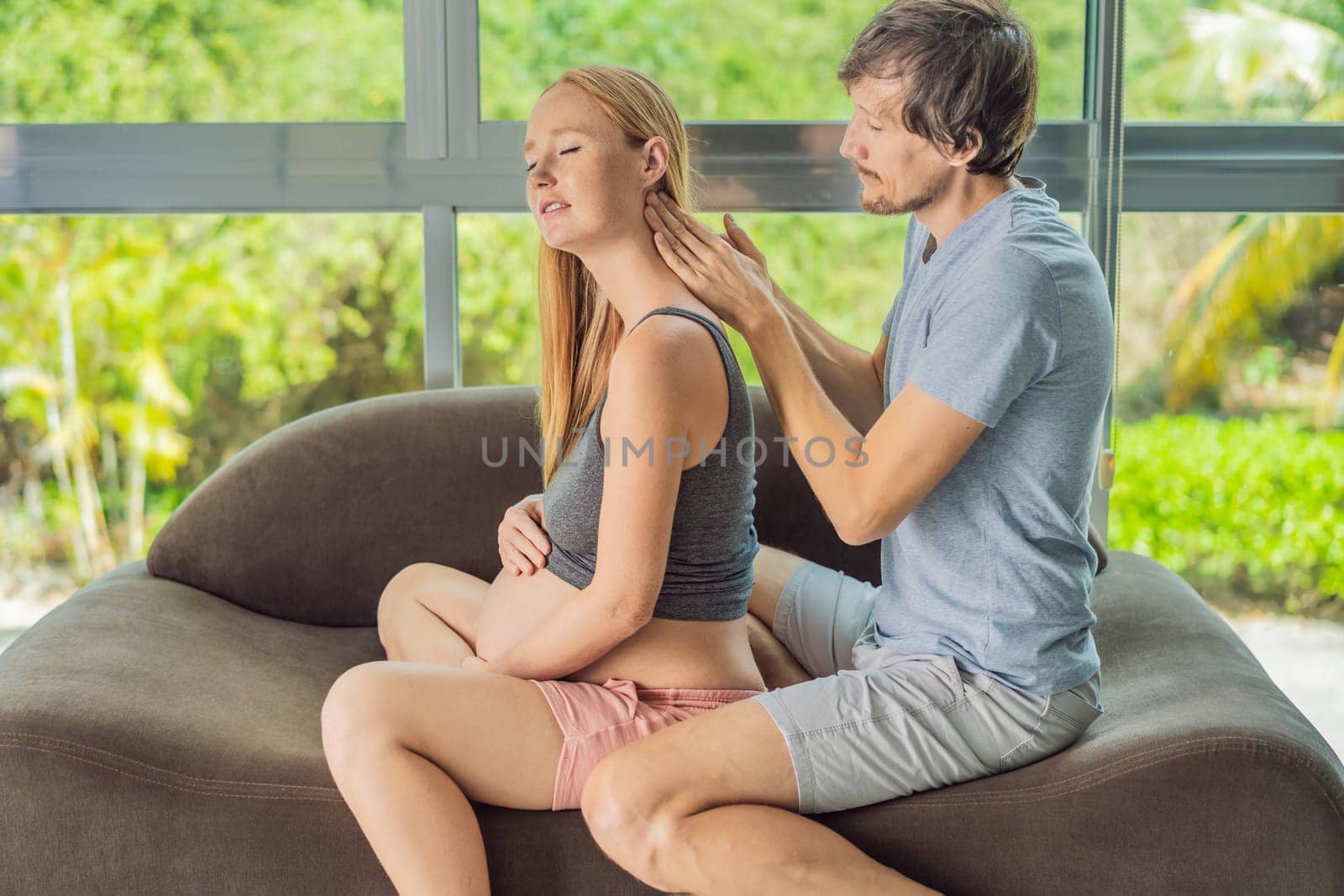 health, pregnancy and happy people concept - husband giving his wife back massage at home by galitskaya
