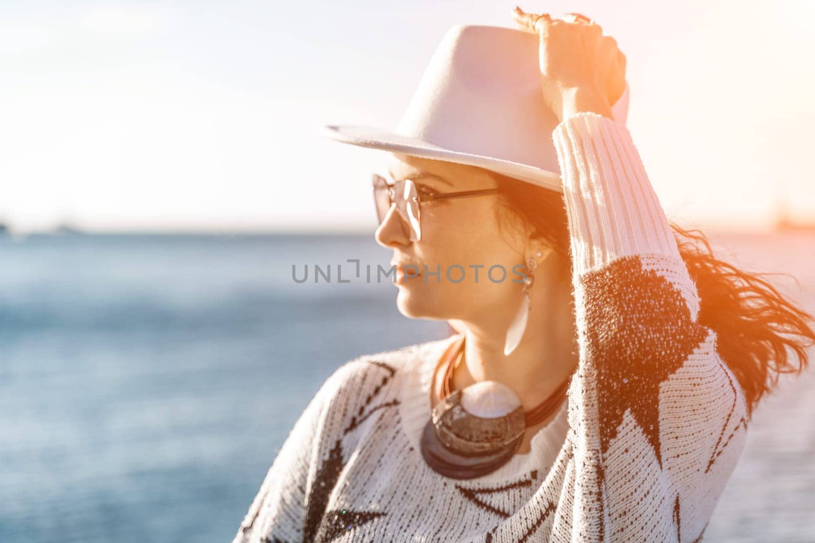 Portrait of a curly haired woman in a white hat and glasses on the background of the sea