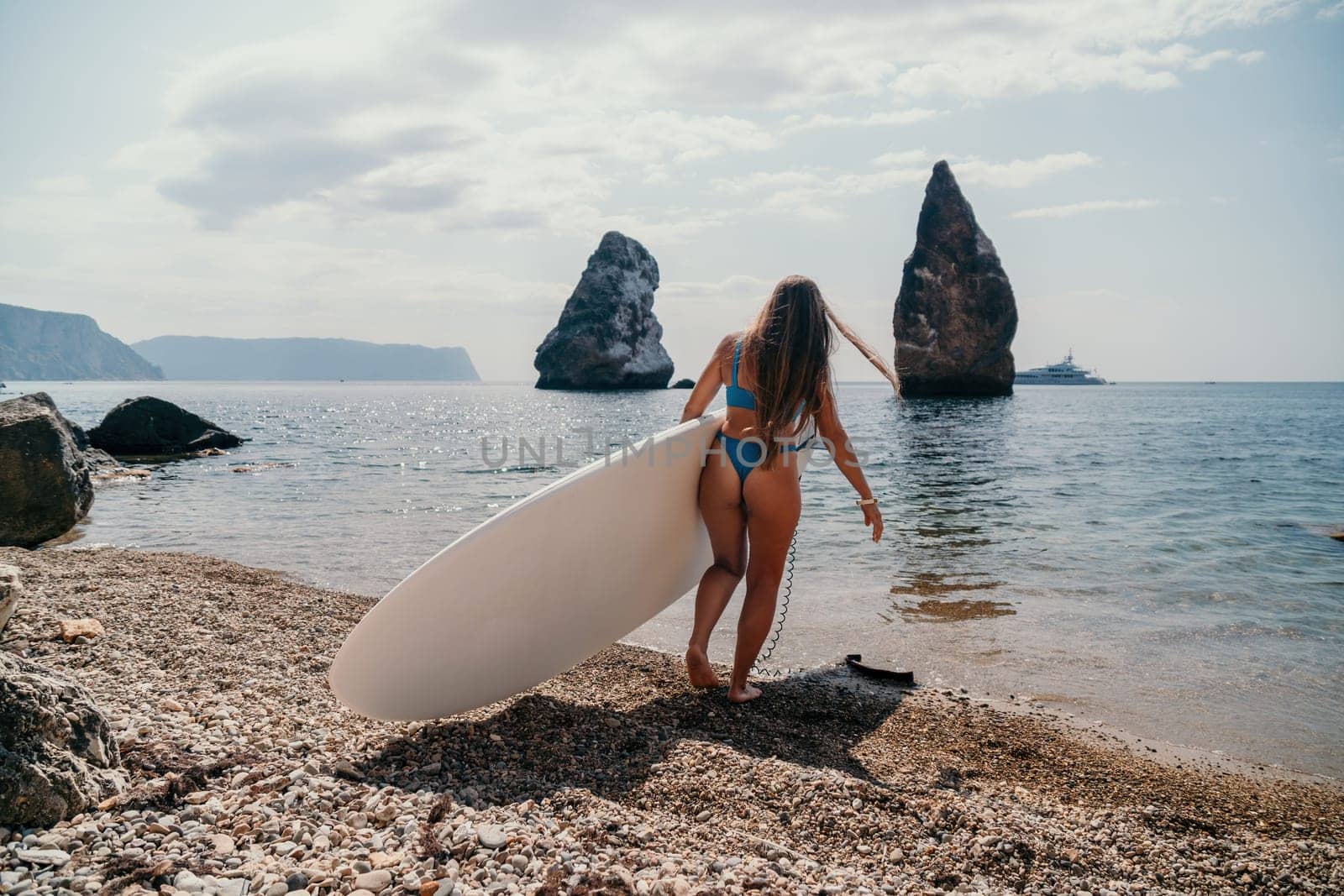 Close up shot of beautiful young caucasian woman with black hair and freckles looking at camera and smiling. Cute woman portrait in a pink bikini posing on a volcanic rock high above the sea