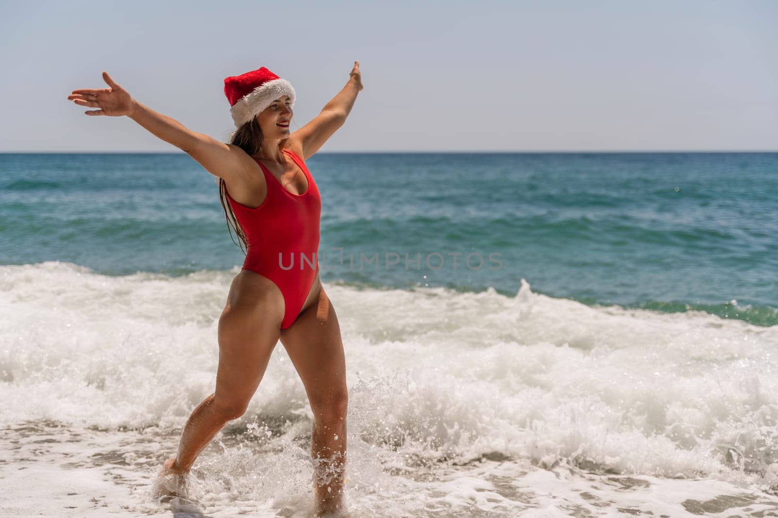 A woman in Santa hat on the seashore, dressed in a red swimsuit. New Year's celebration in a hot country