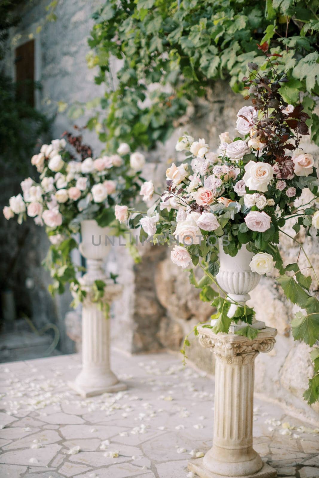 Wedding semi-arch of bouquets of flowers on pedestals near a stone wall in the garden by Nadtochiy