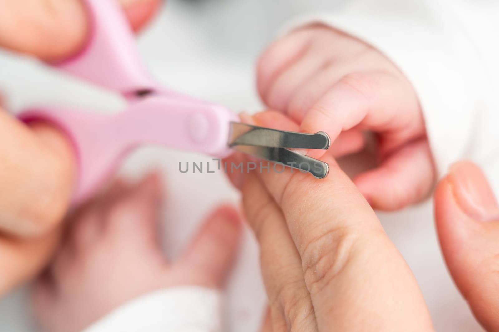 A close-up captures a mother attentively cutting her newborn's fragile nails with small scissors