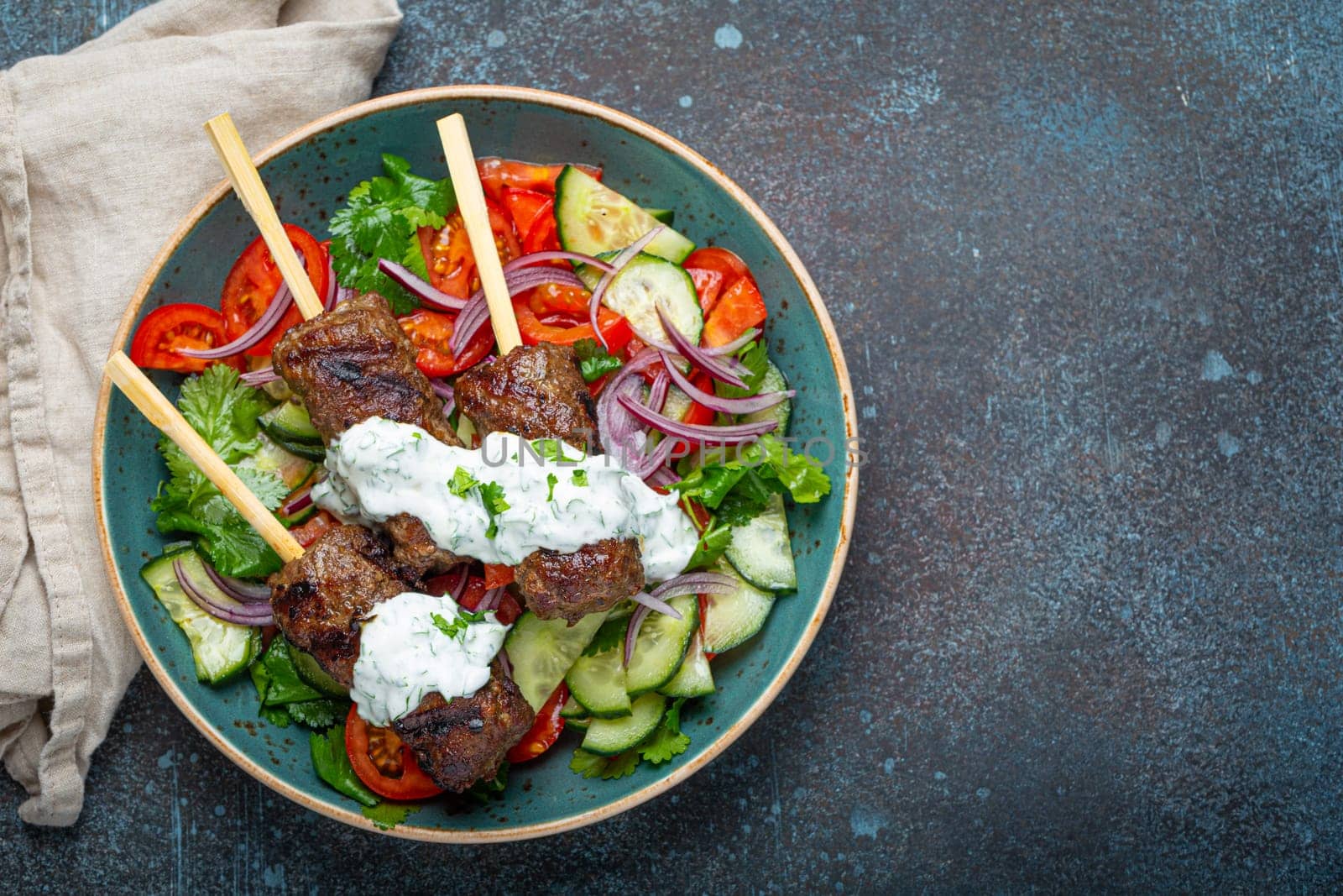 Grilled skewer meat beef kebabs on sticks served with fresh vegetables salad on plate on rustic concrete background from above. Traditional Middle Eastern Turkish dish Kebab, space for text by its_al_dente