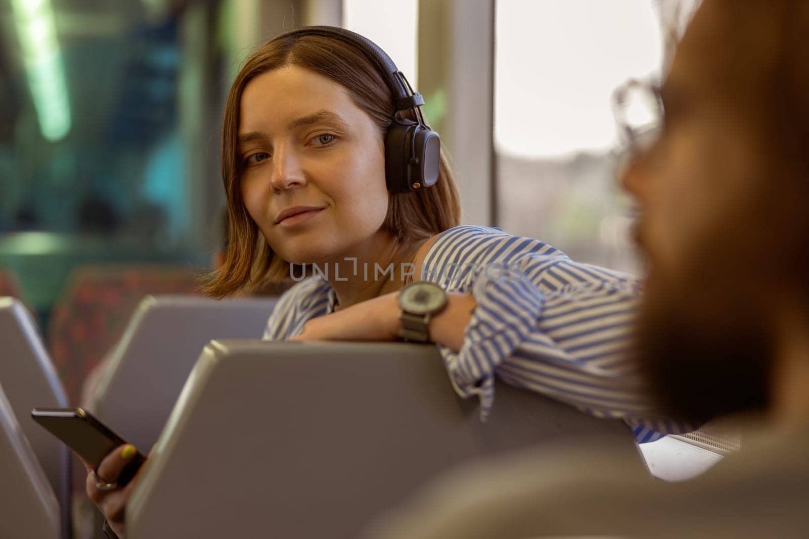Smiling woman in headphones use smartphone while traveling in public transport . High quality photo