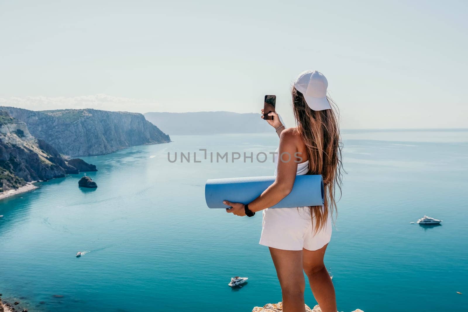 Woman with yoga mat over calm azure sea. Well looking middle aged woman with long hair, fitness instructor with blue yoga mat near the sea. Female fitness yoga routine concept. Healthy lifestyle. by panophotograph