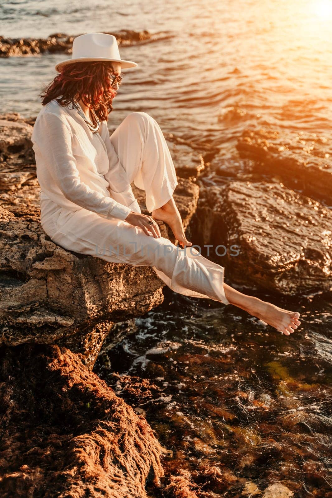 woman sea sunset. woman in a white pantsuit and hat is sitiing on the beach enjoying the sea. Happy summer holidays by Matiunina