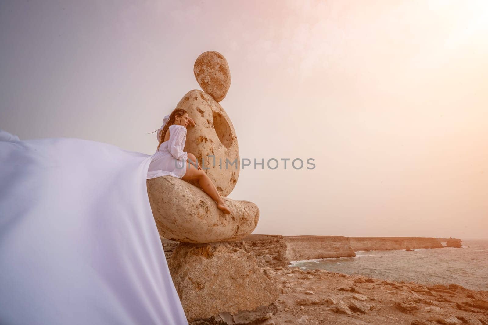 Woman sky stone. Lady stands on stone sculpture with ocean view. She is dressed in a white long dress, against the backdrop of the sea and sky. The dress develops in the wind. by Matiunina