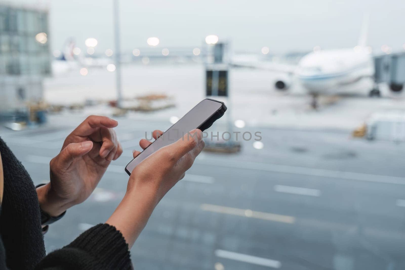 Happy Asian tourist uses mobile smartphone with travel backpack while waiting for flight in airport by wichayada