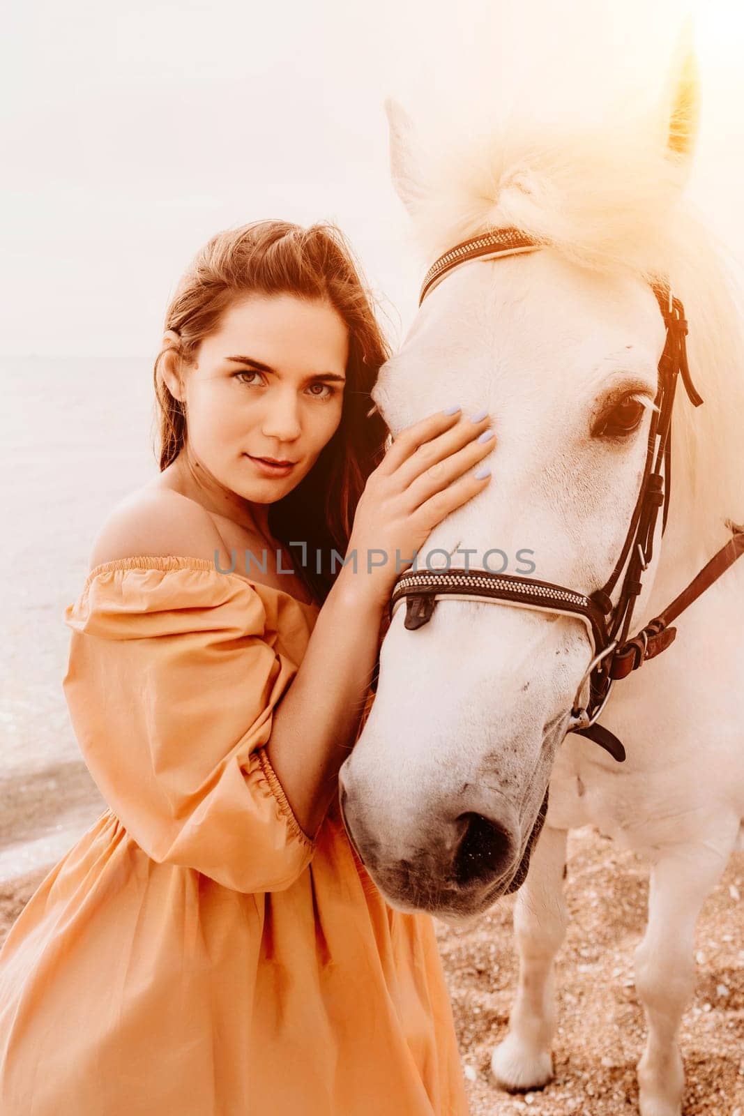 A white horse and a woman in a dress stand on a beach, with the sky and sea creating a picturesque backdrop for the scene