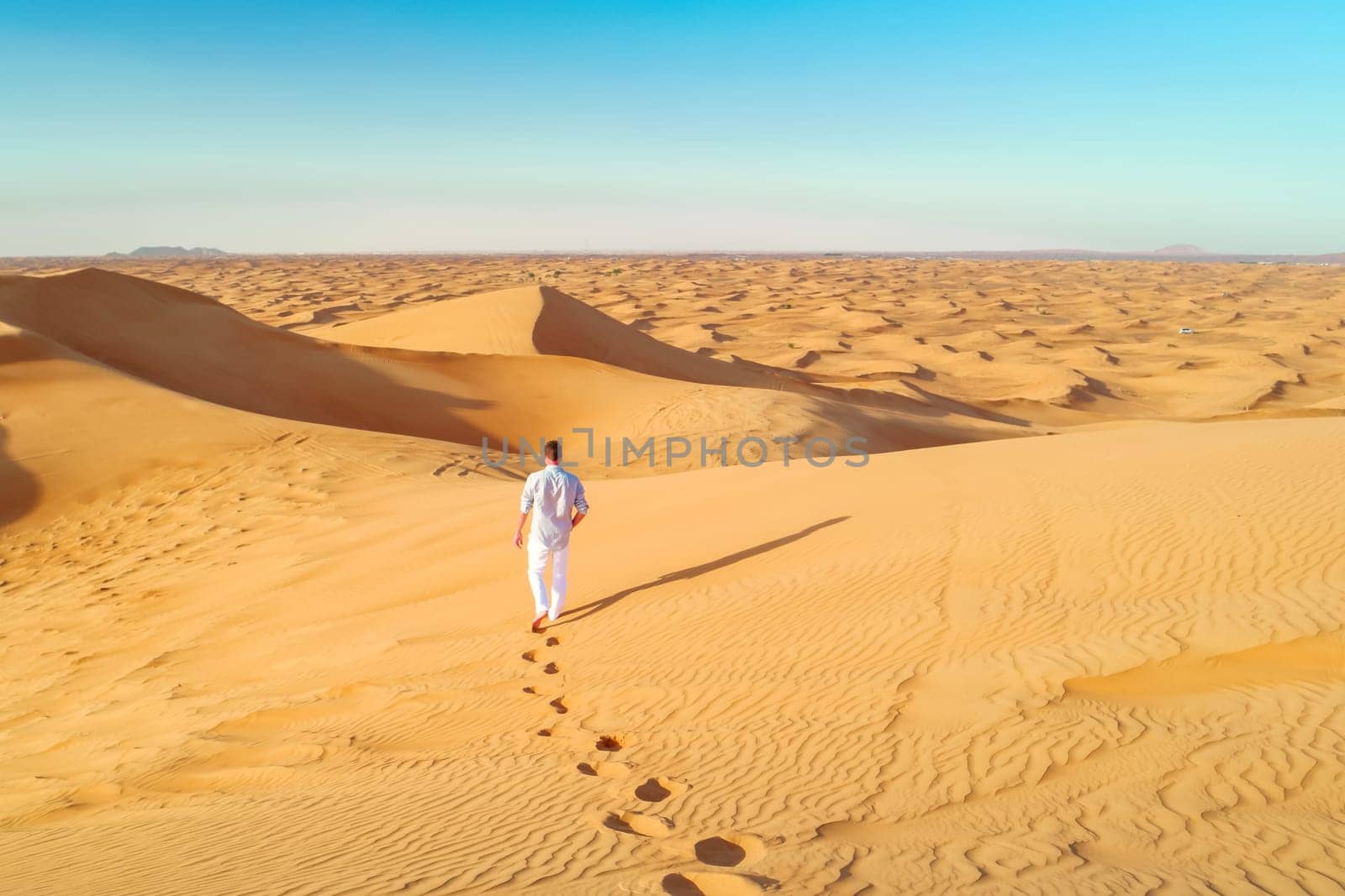Dubai desert sand dunes, young men walking at the sand dunes of Dubai during a desert safari. man walking in the desert of Dubai