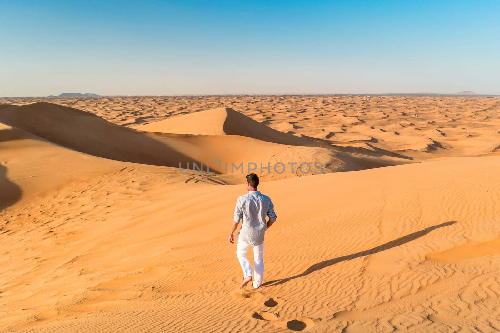 Dubai desert dunes, young men walking at the dunes of Dubai during a desert safari. man walking in the desert sand of Dubai