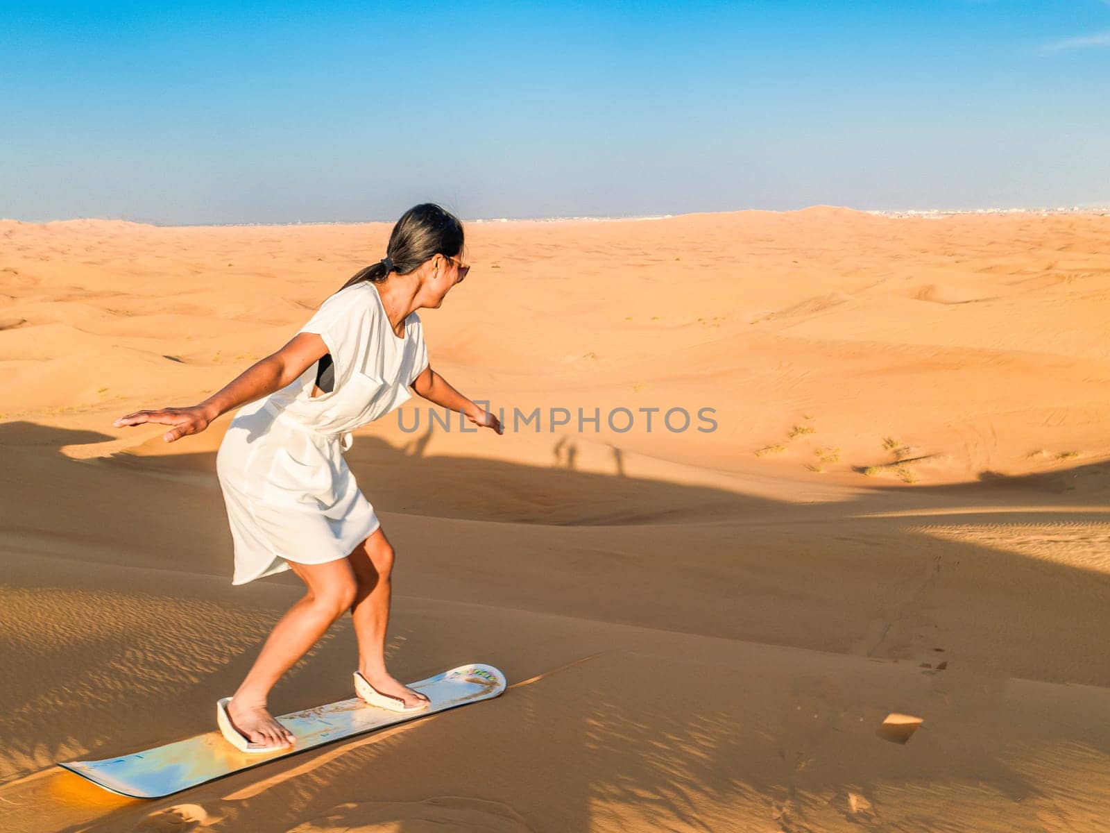 Young Asian women sand surfing at the sand dunes of Dubai United Arab Emirates, sand desert on a sunny day in Dubai.
