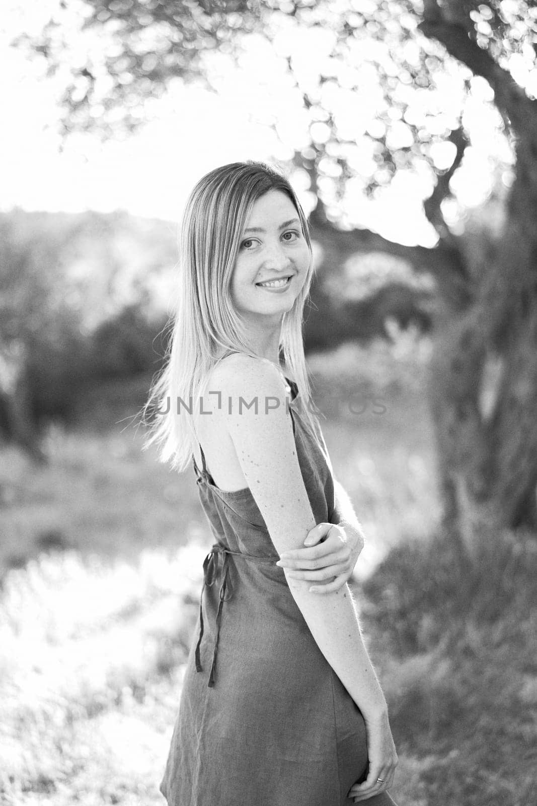 Smiling girl stands half-turned in the park, touching her elbow with her hand. Black and white photo. High quality photo