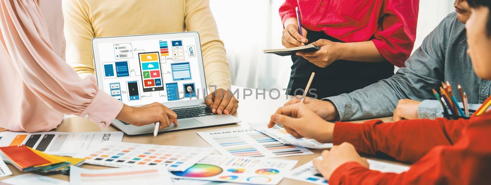 Cropped image of interior designer team presents color by using color swatches while laptop displayed UI and UX designs for mobiles app and website. Creative design and business concept. Variegated.