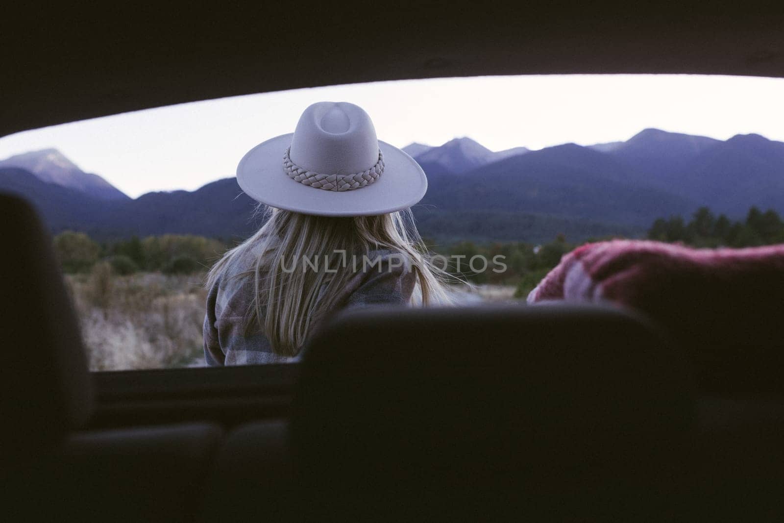 Woman traveler sitting on hatchback car with mountain background