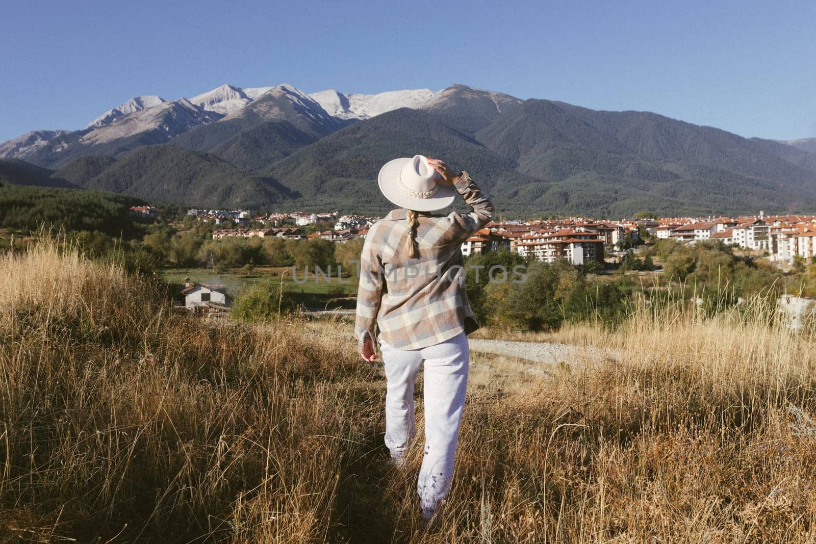 A woman stands in a meadow and looks at the mountains.