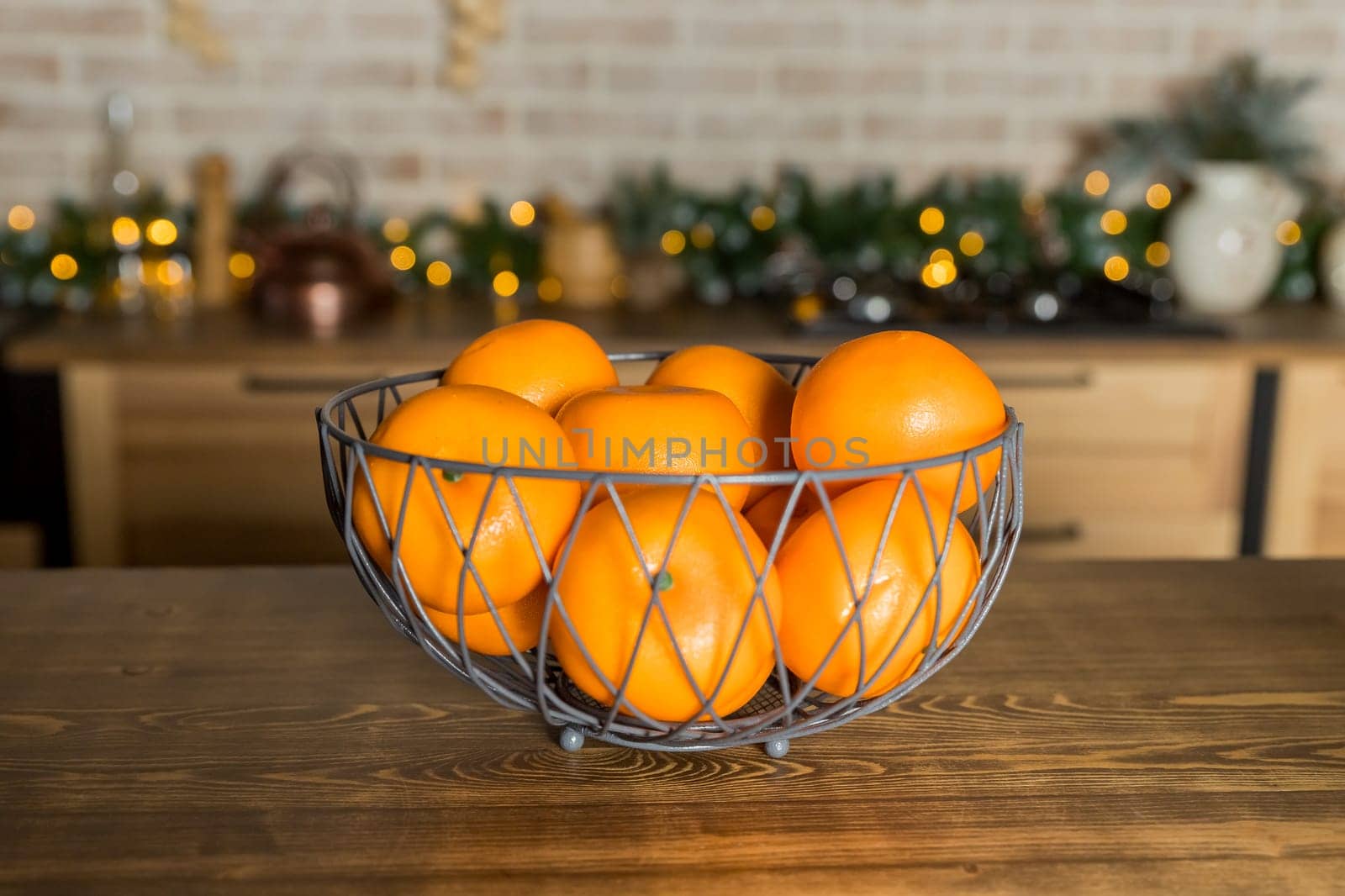 Fresh tangerines in wooden bowl on table against stylish decorated christmas tree with golden lights in scandinavian room.