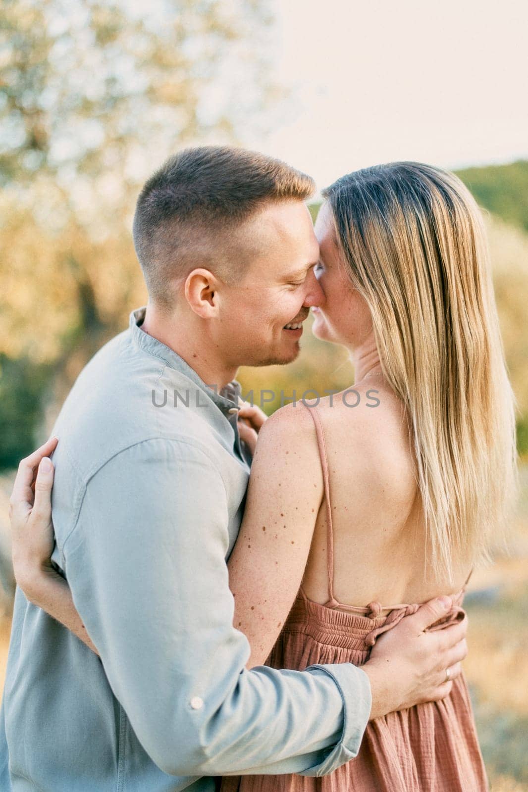 Smiling man hugs woman, touching his nose to her cheek. Back view. High quality photo