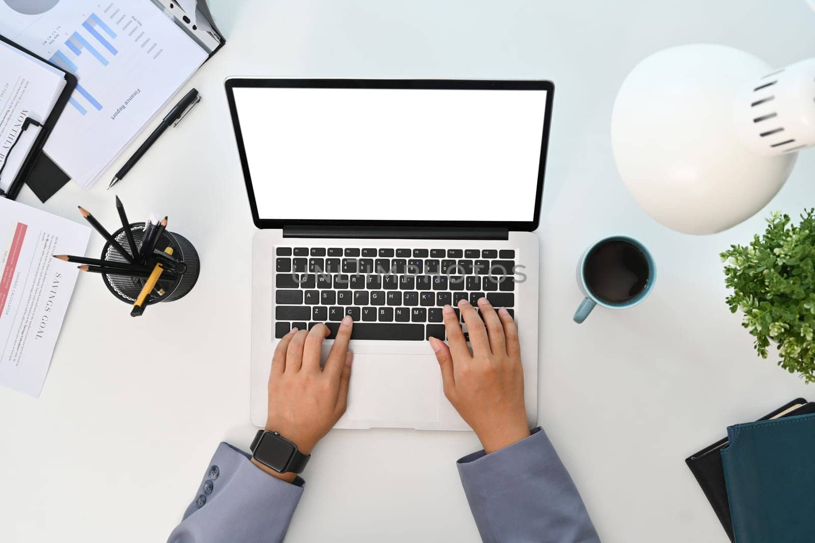 Top view of businesswoman typing on laptop, working at office desk with financial documents.