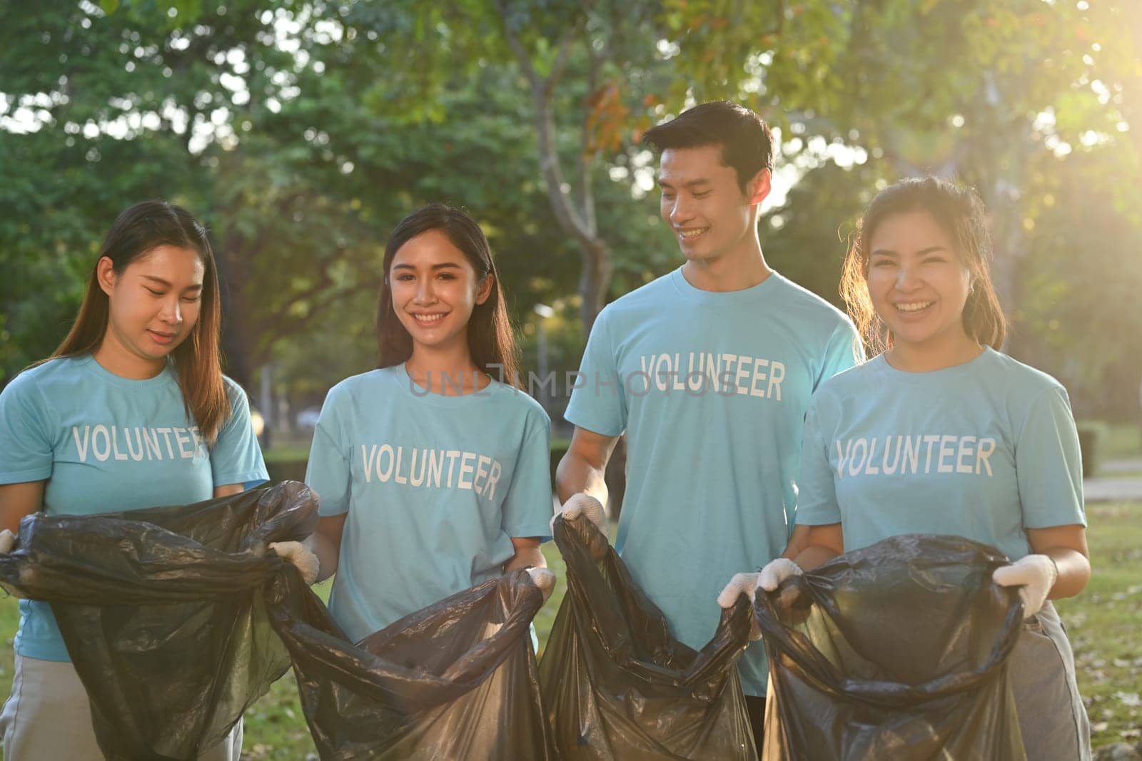 Team of young volunteers with garbage bags cleaning up the forest together by prathanchorruangsak