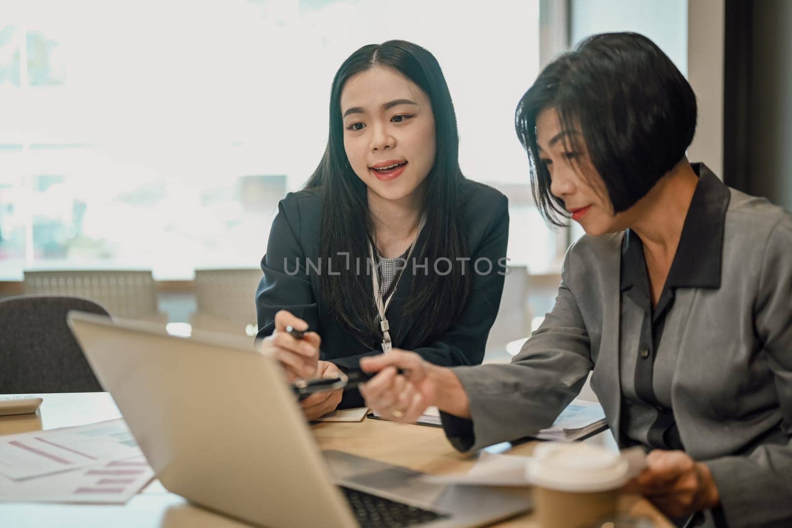 Senior female ceo and young female worker discussing company presentation at meeting table.