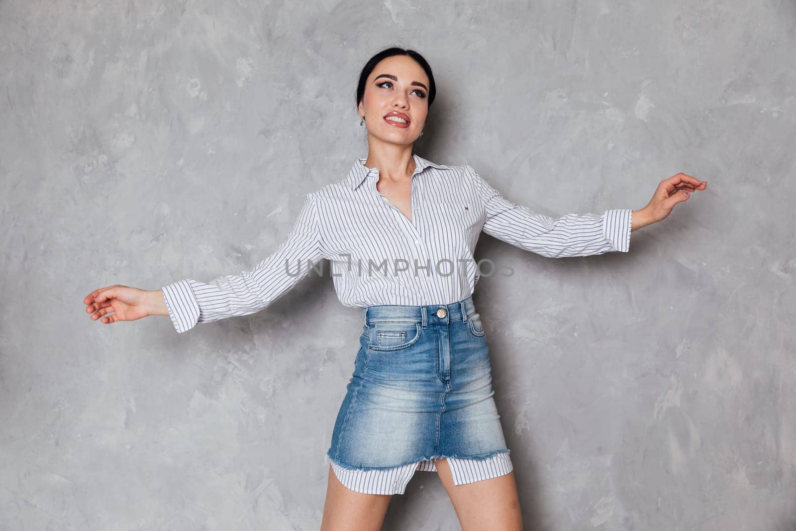 Beautiful fashionable woman in denim skirt posing in studio on gray background by Simakov