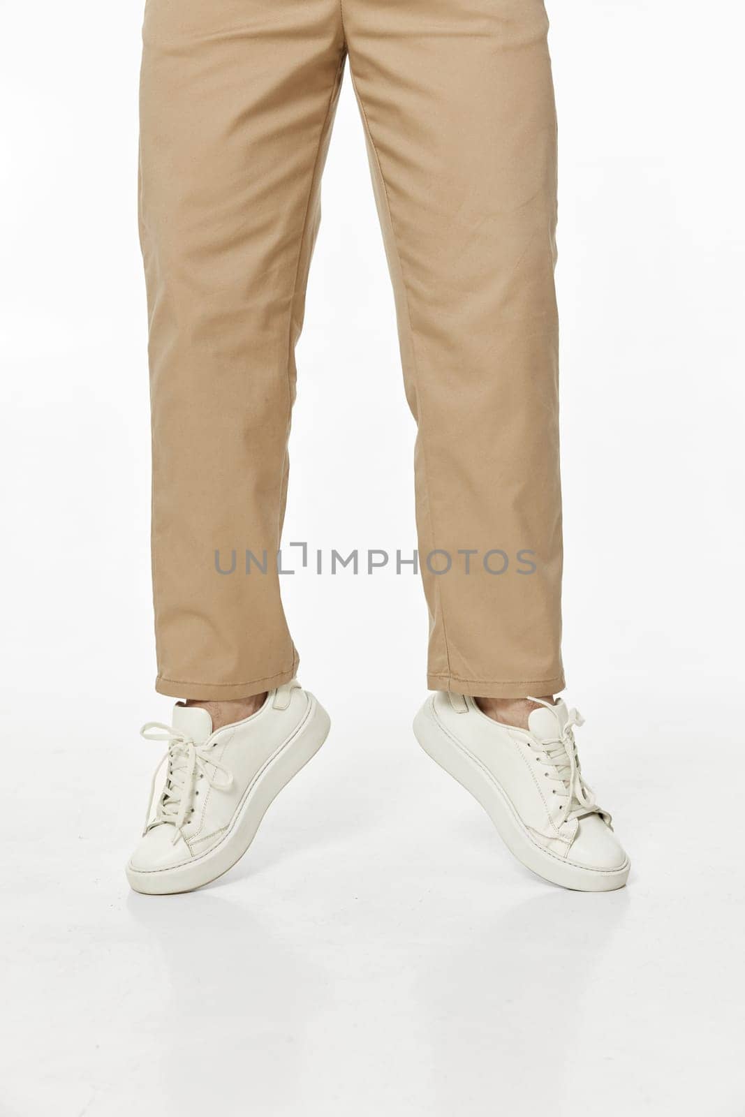 man wearing white sneakers and casual beige pants jumping on studio background, front view