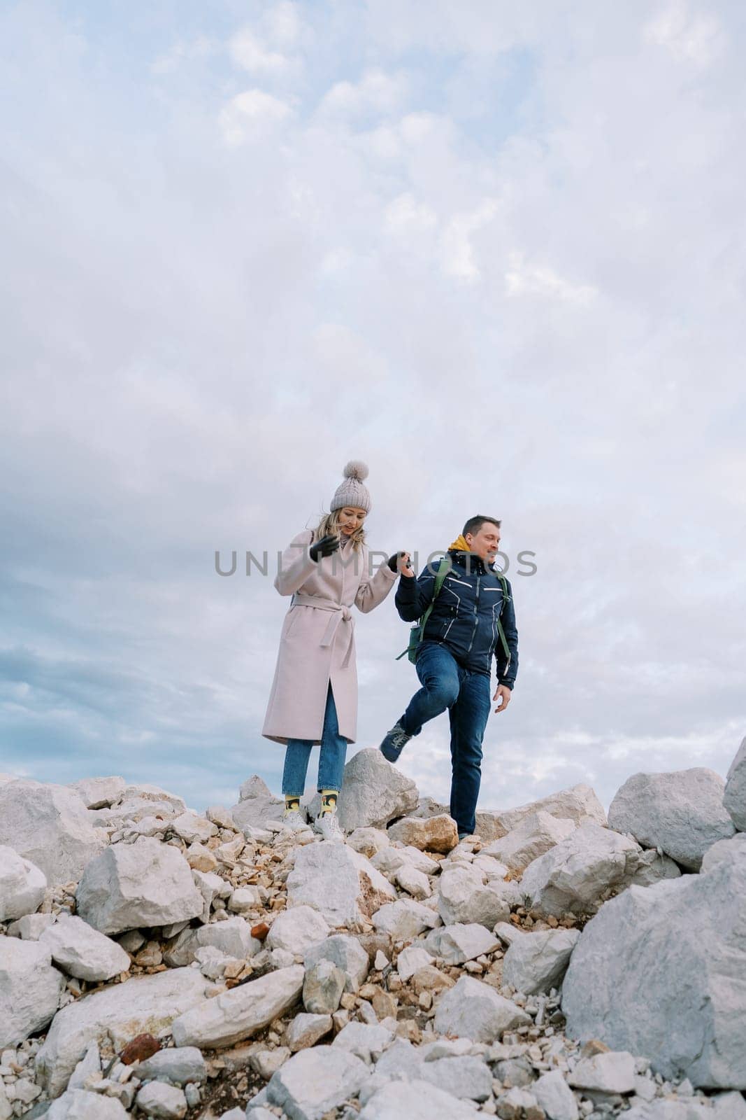 Couple with backpacks walks holding hands over stones against a cloudy sky. High quality photo