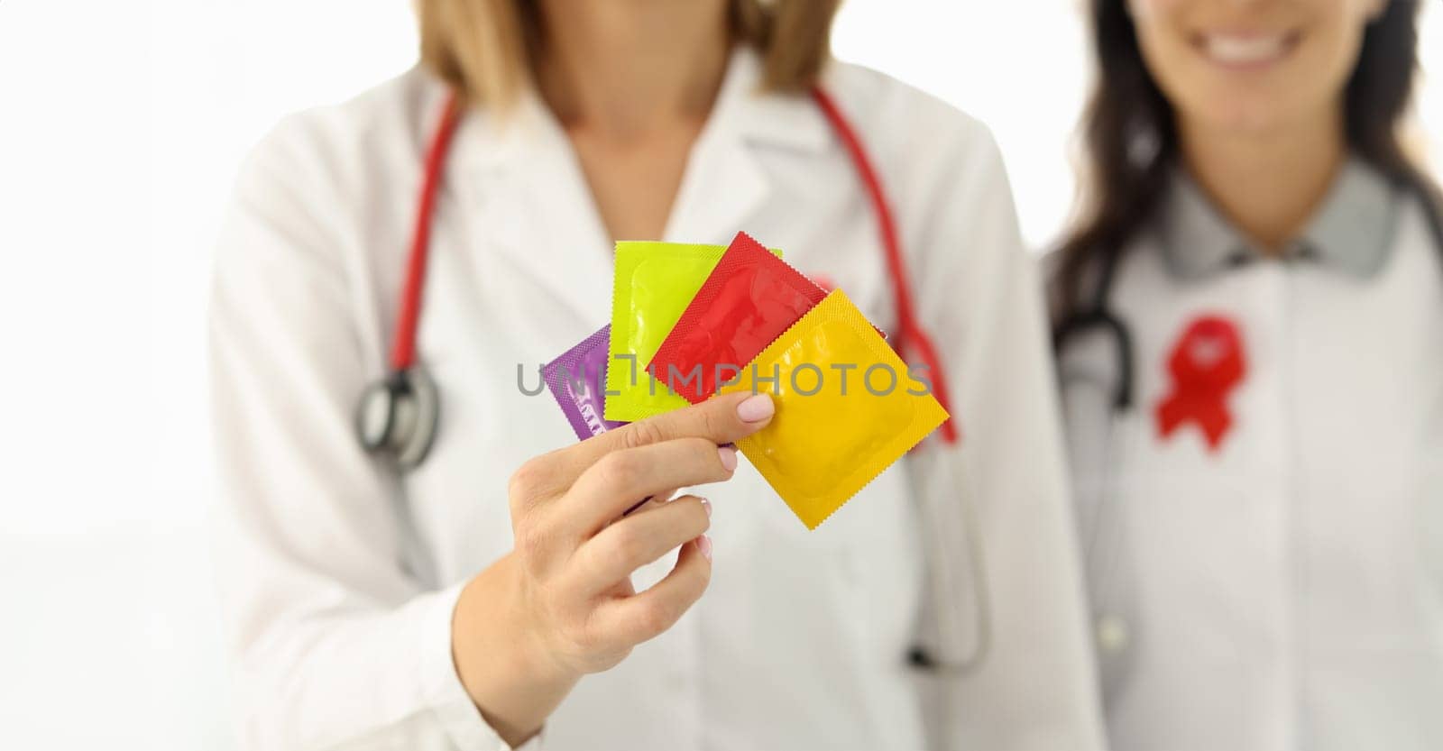 Doctor in white suit hold in hand four condom of different colors. Nurse with red lisbian symbol on her chest.