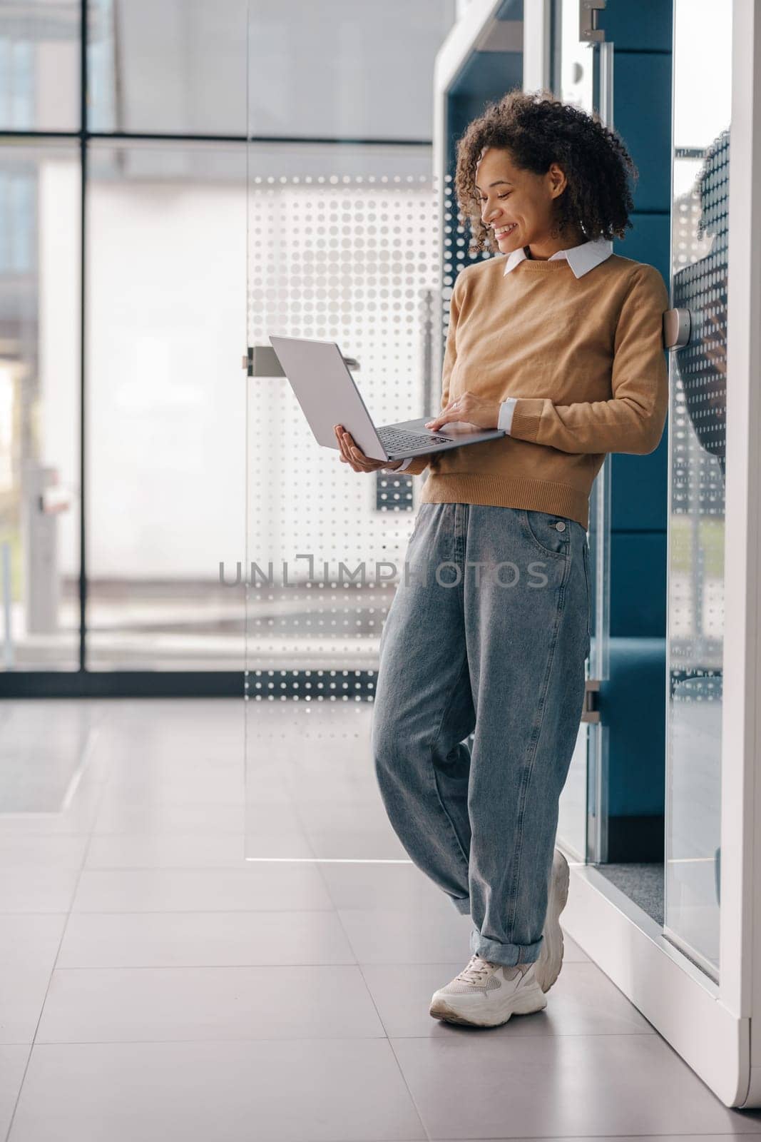 Smiling female freelancer working on laptop while standing on modern coworking background by Yaroslav_astakhov