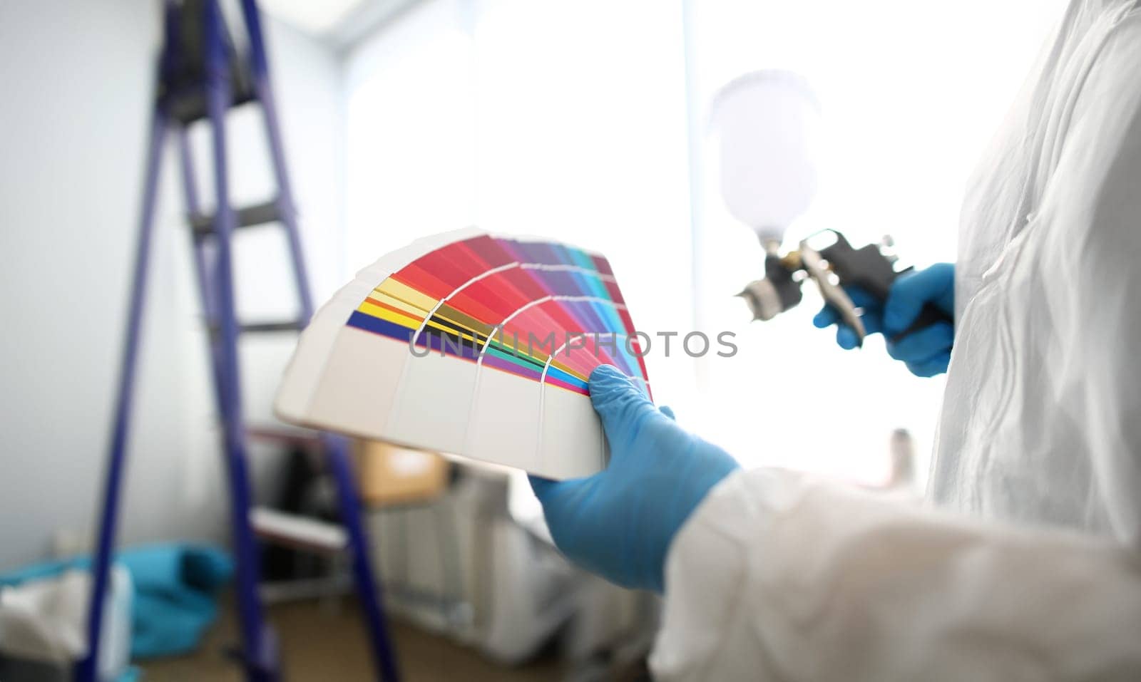 Hands of workman holding airbrush and colorful fantail picking wall tone to paint closeup