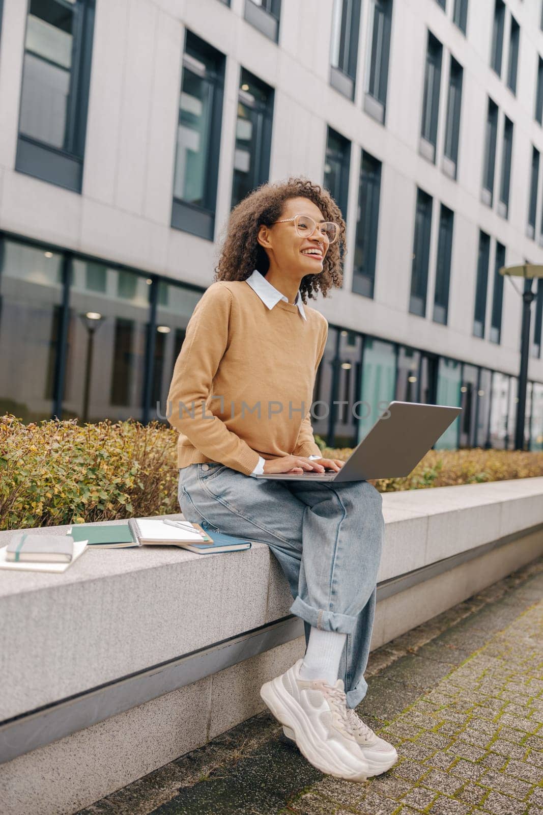 Pretty female entrepreneur working on laptop sitting outside on modern building background