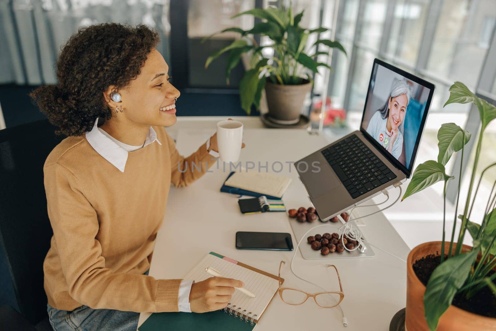 Female freelancer have video conference with client and making notes sitting in cozy coworking