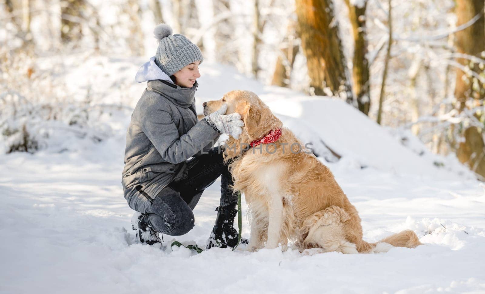 Teenage Girl And Golden Retriever Sit Together In Snow-Covered Forest During Winter