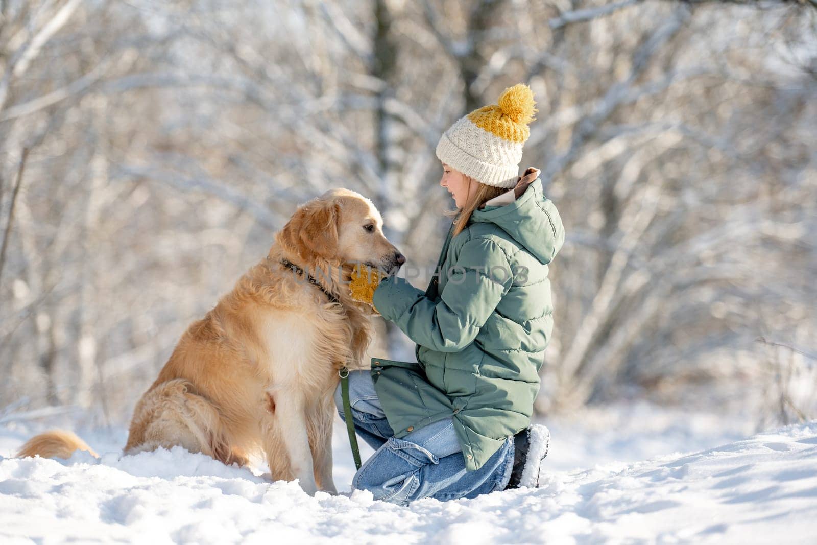 Small Girl And Golden Retriever Sit Together In Snow-Covered Forest During Winter