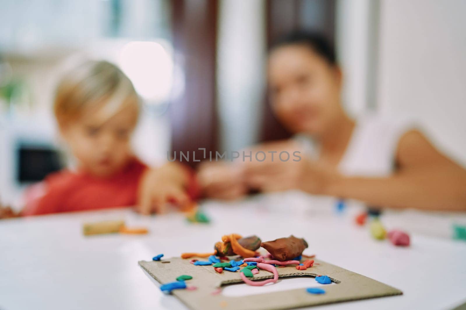 Figurines of various shapes made of plasticine lies on the board against the background of mother and daughter. High quality photo