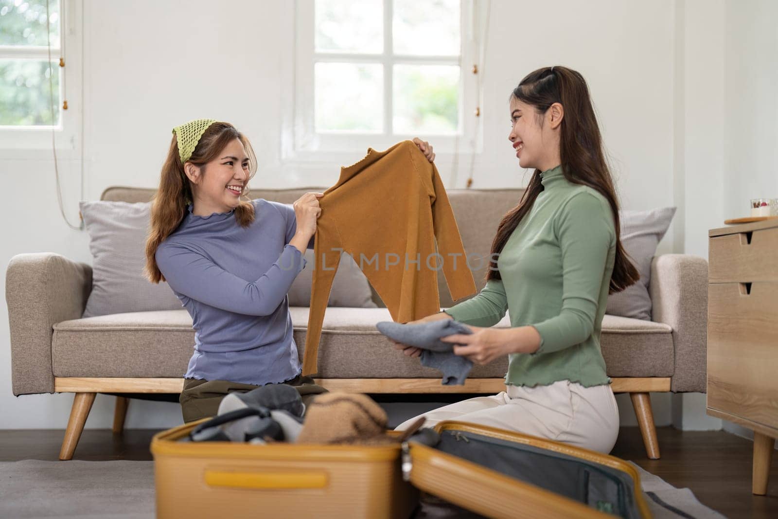 Asian woman prepare to pack clothes travel places with her friends. Asian beautiful two women friend pack things in your travel bag for holidays for her vacation trip.