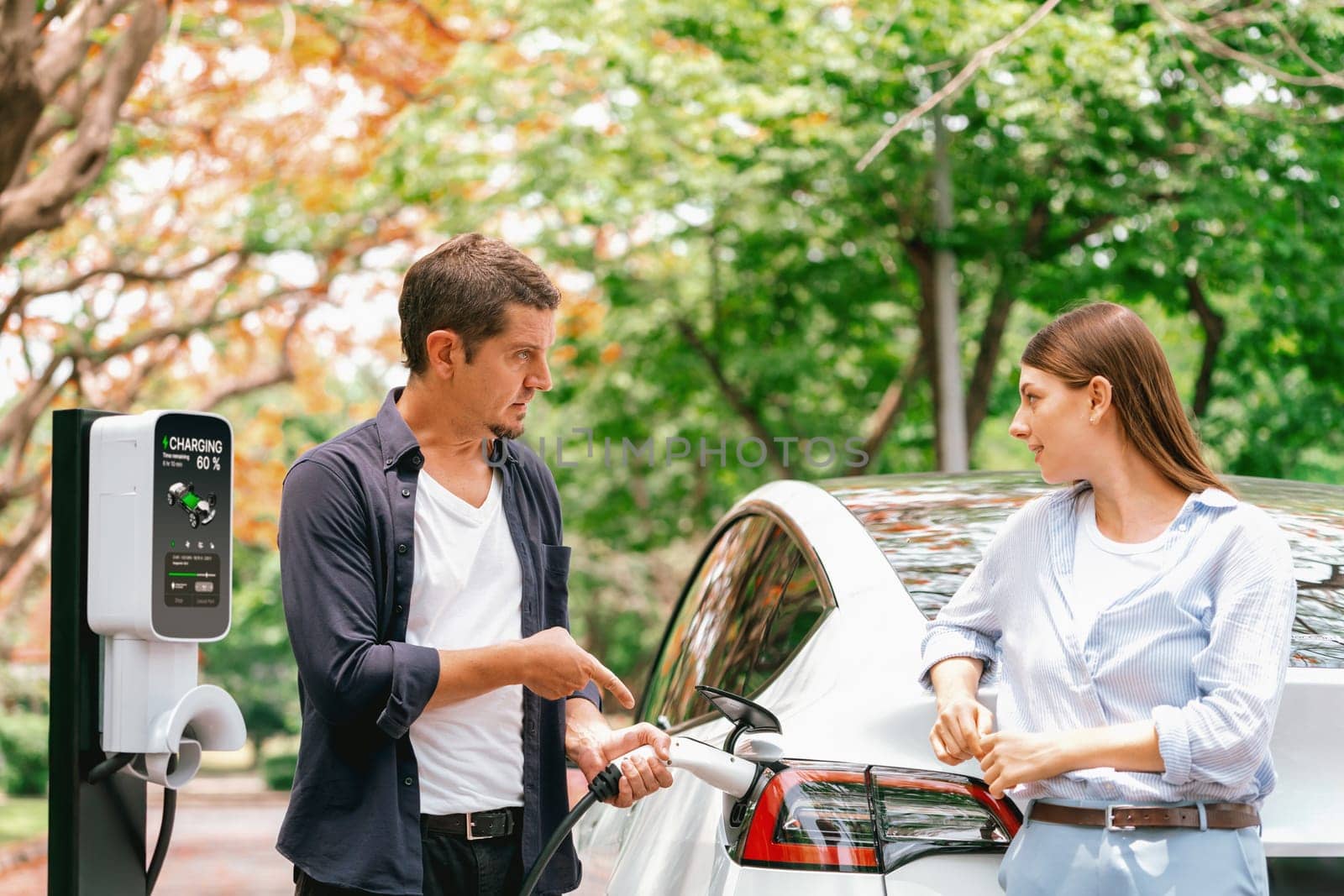 Lovely young couple recharging battery for electric car in autumn. Exalt by biancoblue