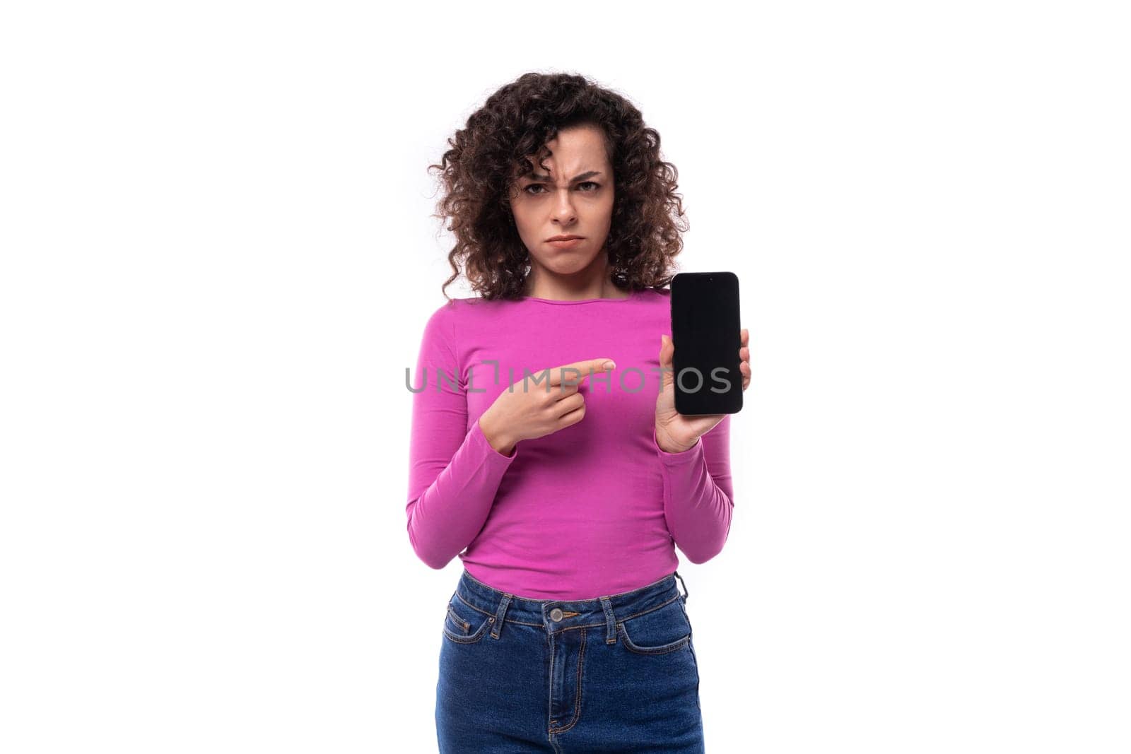stylish slim young curly brunette woman dressed in a lilac turtleneck points her finger at the phone screen.