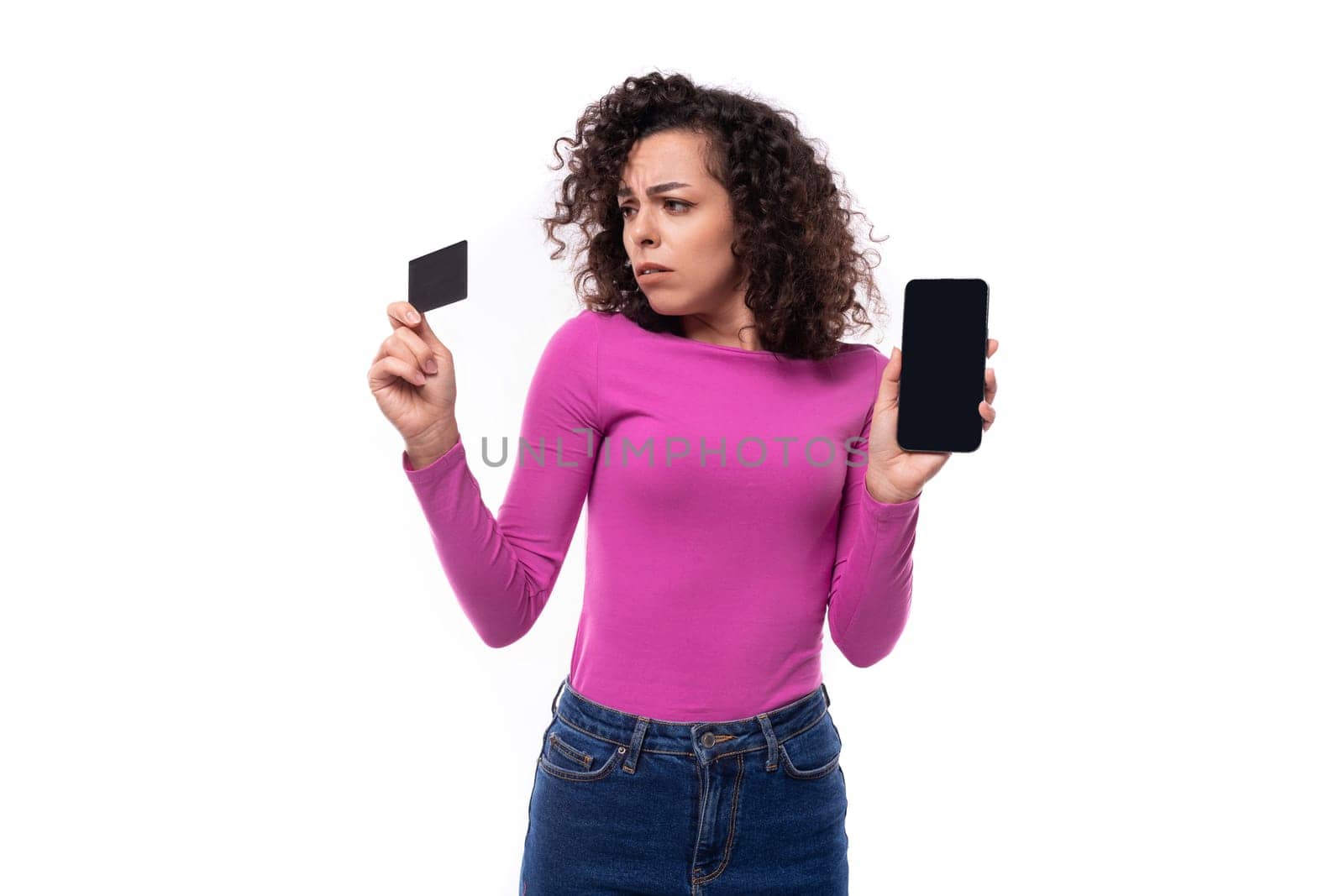stylish slim young curly brunette woman dressed in a lilac turtleneck holds a credit card and a smartphone.