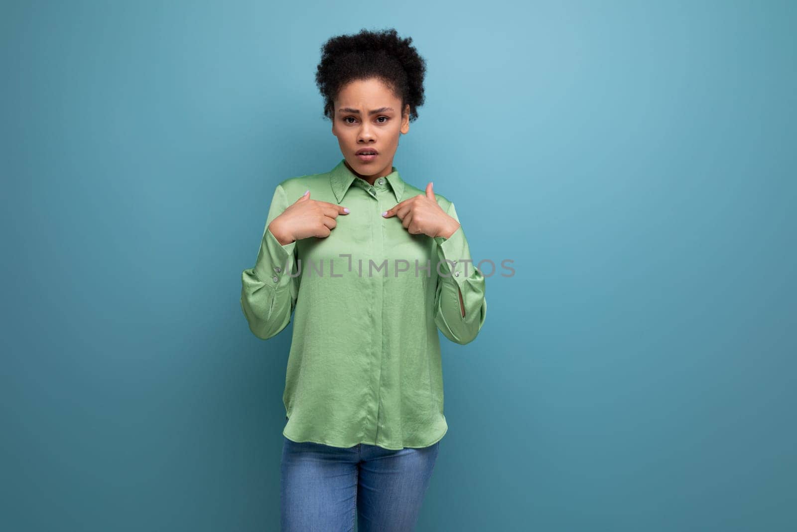 young brunette hispanic woman with curly hair in a green blouse on a blue background with copy space.