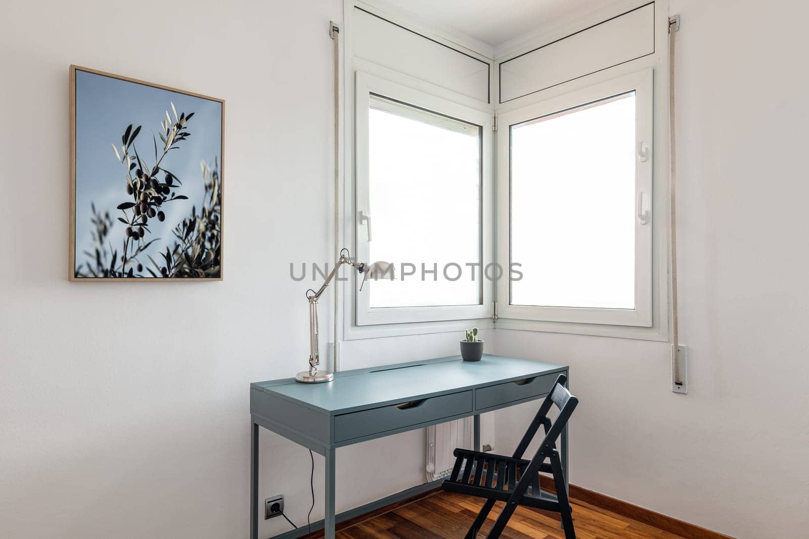 Desk with lamp and chair by corner windows in apartment by apavlin